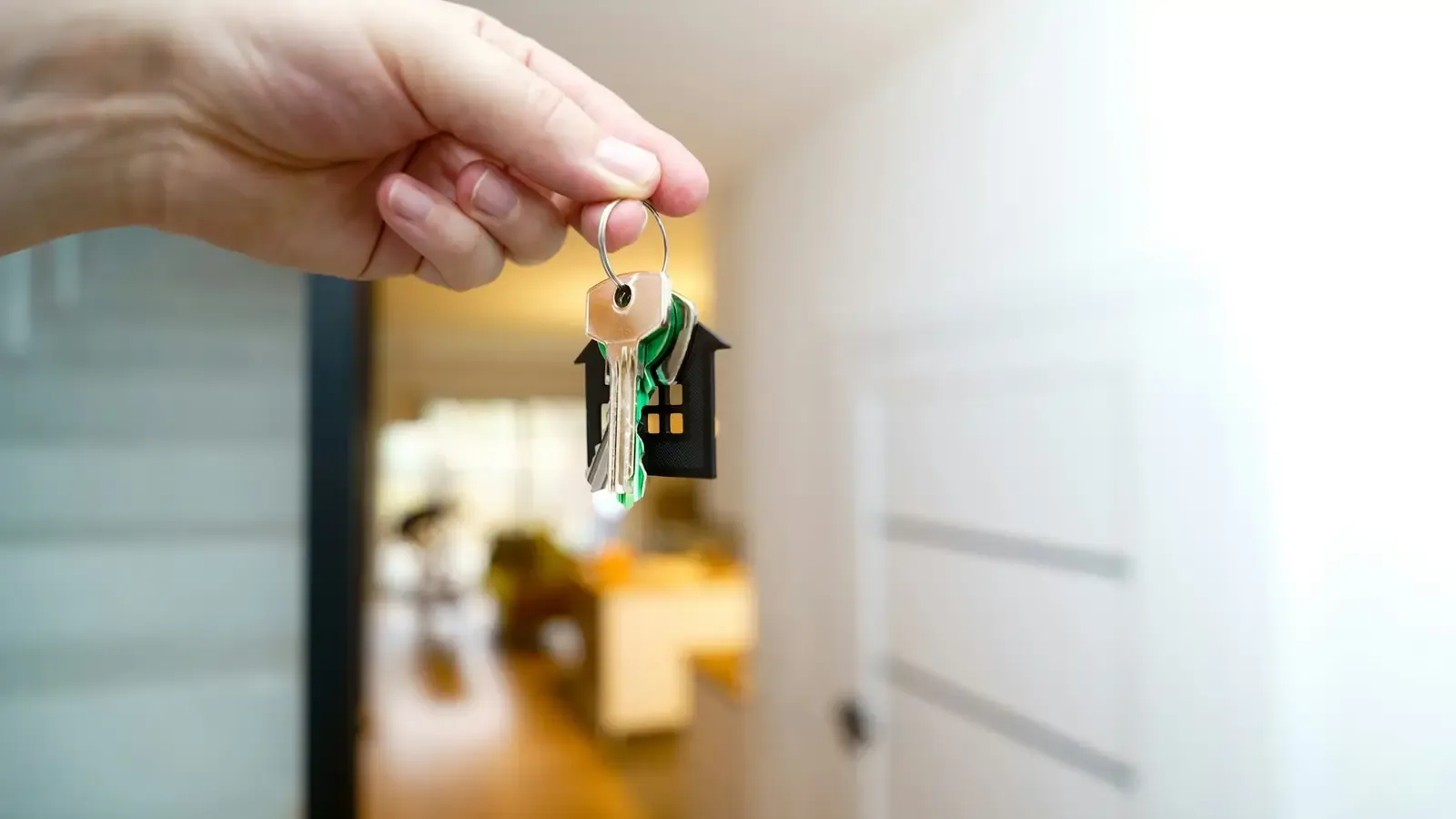 Hand met een sleutelbos en een huisvormige sleutelhanger in een woning